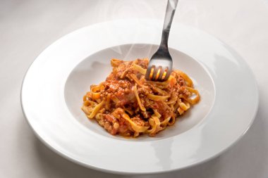 Etli ve domates soslu whit fork ile kaplanmış, beyaz arka planda bir tabakta buğulanmış spagetti yumurtası (İtalyan tagliatelle).