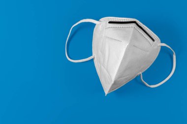 Mavi arka planda beyaz KN95 veya FFP2 maskesi. Coronavirüs salgınını önlemek için Covid-19 koruma maskesi