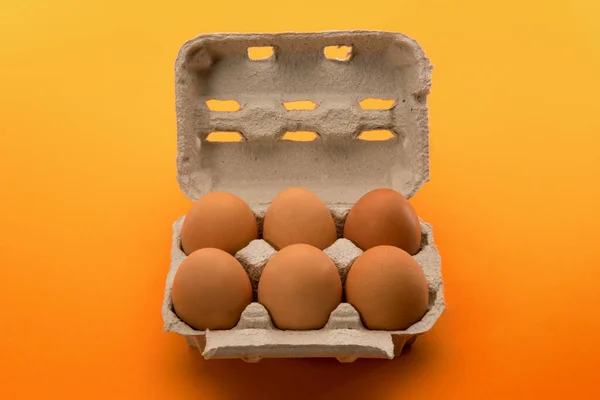 Egg box with eggs, six chicken eggs in cardboard egg tray made from recycled paper isolated on yellow orange background