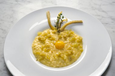 Risotto, devedikeni ve yumurta beyaz tabakta, mermerin üstünde.