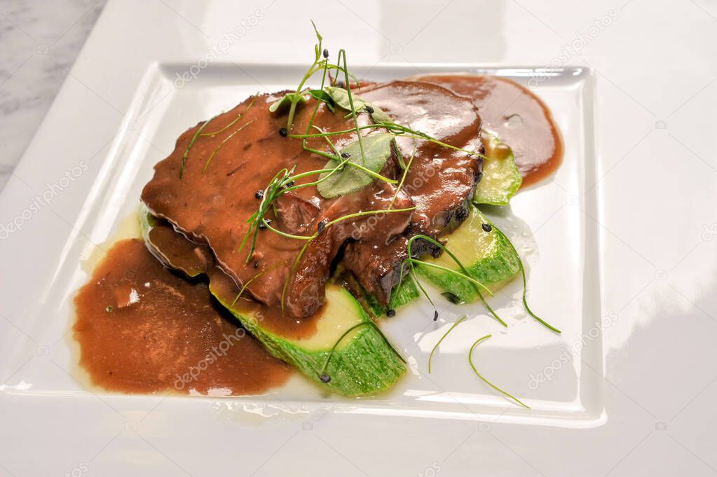 Braised veal in red Barolo wine with a side dish of zucchini and sprouts, in a white plate in top view
