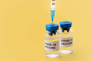 Coronavirus COVID-19 aşısı. Sarı arkaplanda izole edilmiş şırınga şişeleri, kopyalama alanı ile konsept bileşimi 