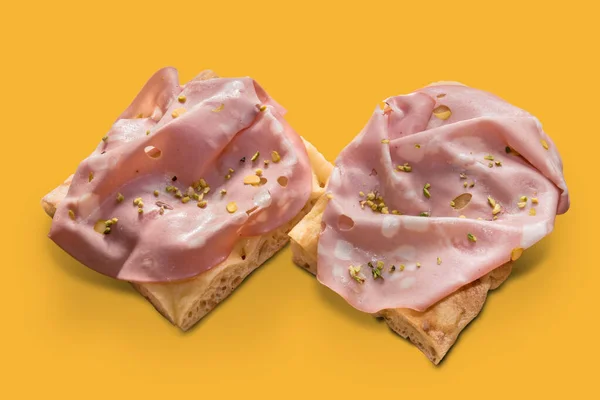 Focaccia ekmeği üzerine İtalyan Bologna Mortadella, doğranmış şam fıstığı, sarı arka planda iki dilim.