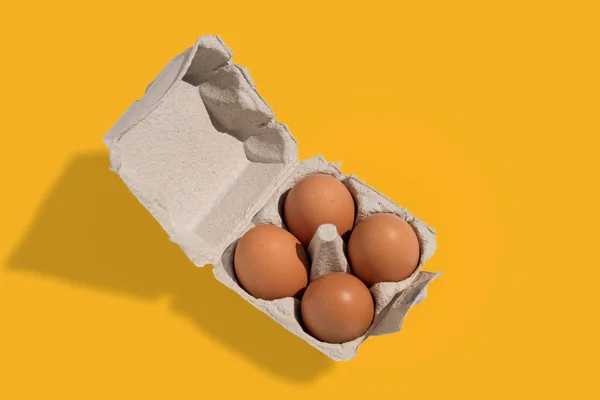 Egg box with eggs, four chicken eggs in cardboard egg tray made from recycled paper isolated on yellow background