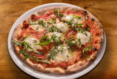 Arugula yapraklı pizza, domates sosu, ahşap masada beyaz tabakta mozzarella peyniri.