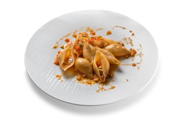 İtalyan makarnası konchiglioni, domates sosu ve beyaz tabakta izole edilmiş sebzelerle pişirilir.