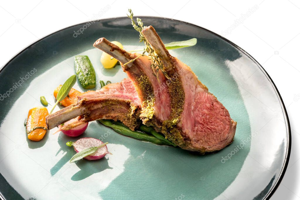 Crusted lamb ribs cutlets with bone in green dish with carrot, radishes and courgette, close up