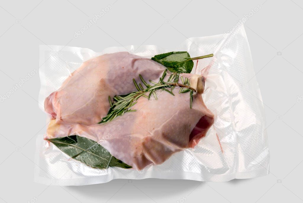 Chicken thighs in vacuum packed sealed for sous vide cooking with rosemary, bay leaf and sage, isolated on light grey background