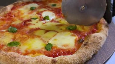 Domates soslu Margherita pizzası, mozzarella ve fesleğen. Kesici tekerlekle kesilmiş.