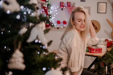 Güzel, genç, sarışın bir kız mutfakta beyaz gömlekli ve kot pantolonlu. Mutfak yeni yıl dekoruyla süslenmiş. Yeni yıla az kaldı..