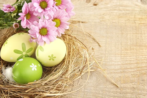 Œufs de Pâques dans le nid avec des fleurs sur une planche de bois — Photo