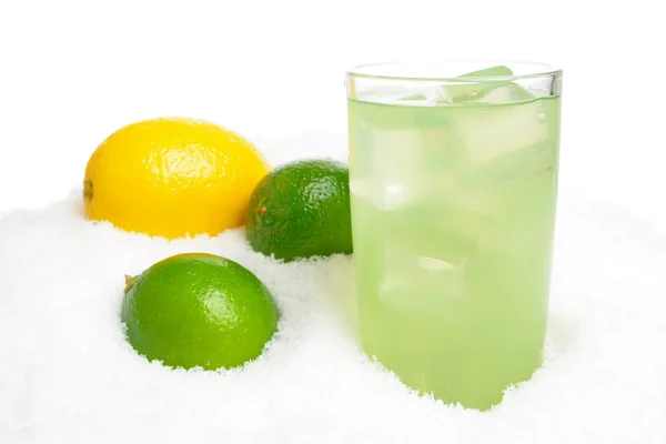 Стакан лаймового сока с кубиками льда, лаймами, лимоном на снегу на белом — стоковое фото