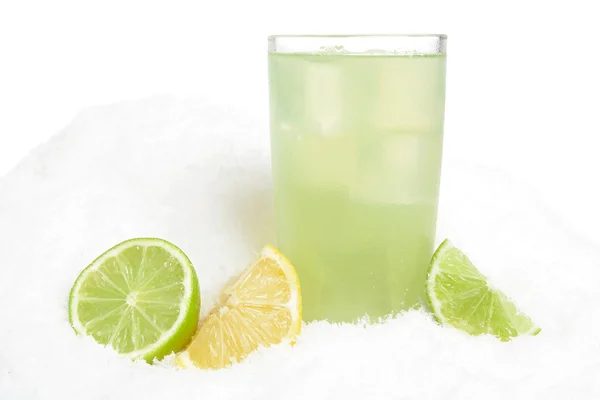 Стакан лаймового сока со льдом кубики, лаймы и лимоны половинки на снегу на белом — стоковое фото