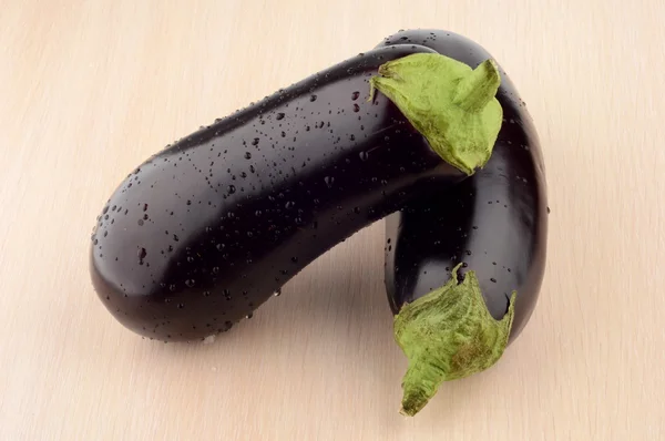 Photo pair wet aubergines eggplants on bright wooden table — Stock Photo, Image