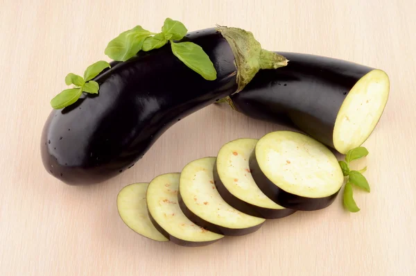 Sliced aubergine, eggplant with basil leaves on bright wooden table — Stock Photo, Image