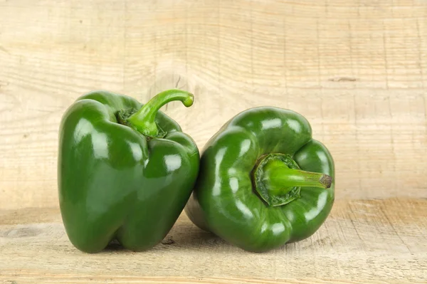 Close-up shot of two green bell peppers on wooden plank — Stock Photo, Image