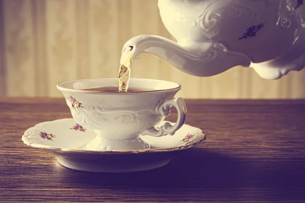 Old-fashioned pouring tea to cup on old wallpaper background — Stock Photo, Image