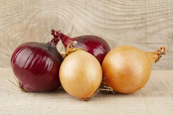 Zwiebeln und rote Zwiebeln auf hölzernem Hintergrund — Stockfoto
