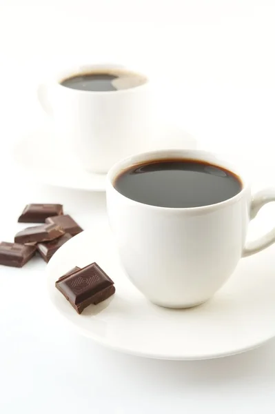 Tazze di caffè con cioccolato e piattini su bianco — Foto Stock