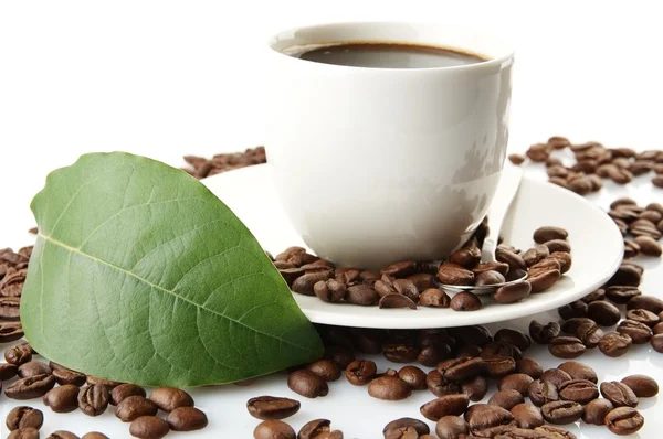 Scattered coffee beans with cups of coffee and leaf — Stock Photo, Image