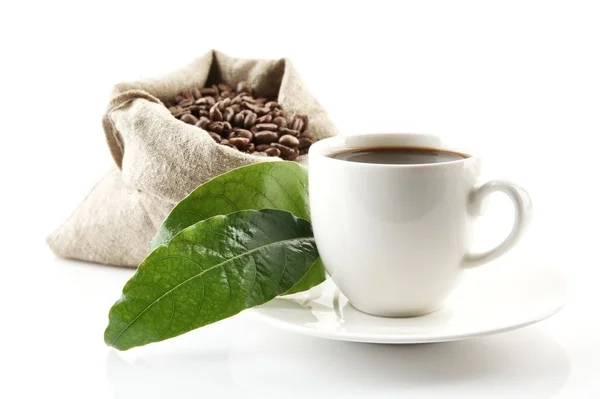 Мешок, полный кофейных зерен с зелеными листьями и чашкой кофе — стоковое фото