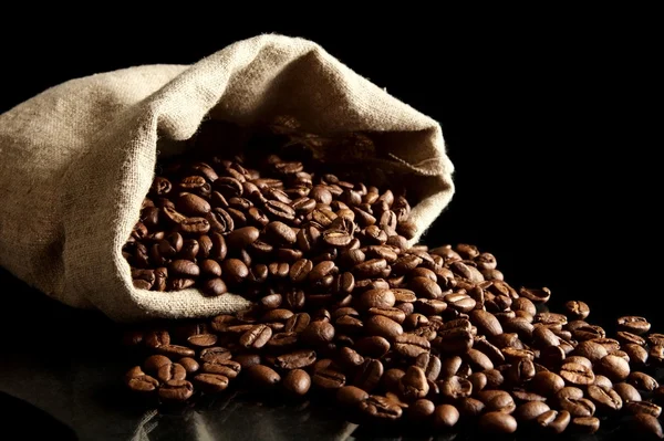 Overturned bag full of coffee beans on black — Stock Photo, Image