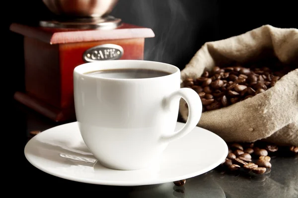 Kopje koffie met molen, zak vol met koffiebonen op zwart — Stockfoto