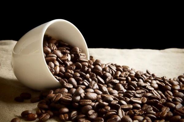 Strödda bönor kaffe från en kopp på svart och lin — Stockfoto