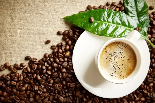 Coffee with foam cup with beans in the corner with green leaf on flax — Stock Photo, Image