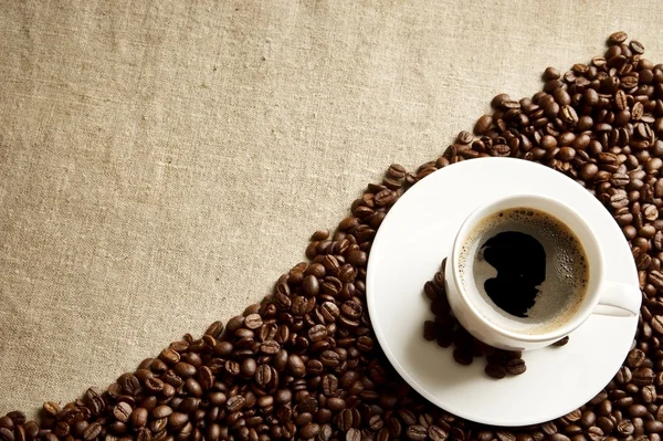 Schuimige koffiekopje met bonen in de hoek op stof vlas — Stockfoto