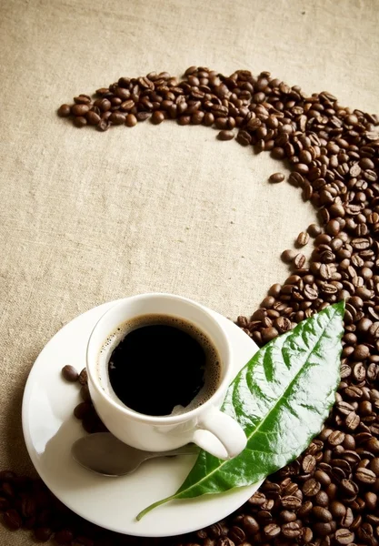 Taza de café con frijoles retorcidos en un remolino sobre textil de lino —  Fotos de Stock