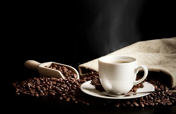 Cup of coffee with bag with coffee beans on black desk — Stock Photo, Image