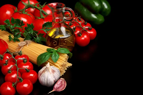 Pasta raw isolated on black with tomatoes,olive oil,garlic left — Stock Photo, Image