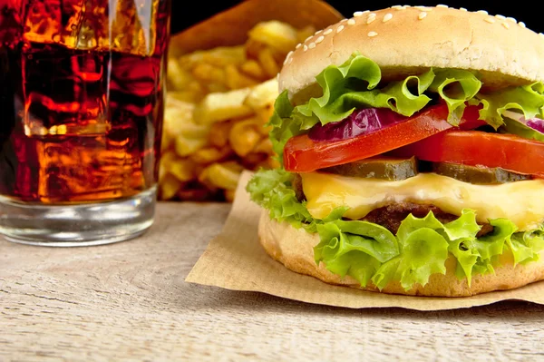 Grote interne cheeseburger met glas cola en frietjes op houten bureau op zwarte achtergrond — Stockfoto