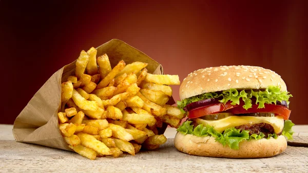 Cheeseburger, batatas fritas no fundo vermelho na prancha de madeira — Fotografia de Stock