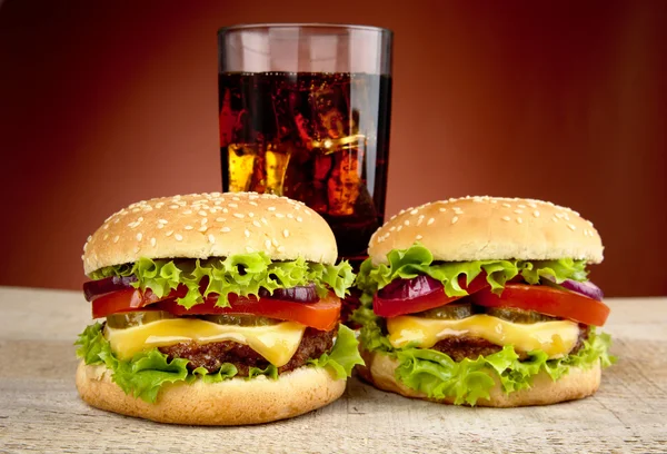 两个芝士汉堡与玻璃的红色背景上的木桌上的可乐 — 图库照片