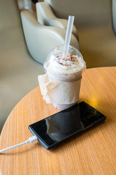 Recharge de téléphone portable dans le café avec une tasse en plastique de frappe au chocolat glacé — Photo