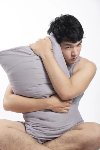 Asian man in grey pajamas sitting and holding the pillow — Stock Photo, Image