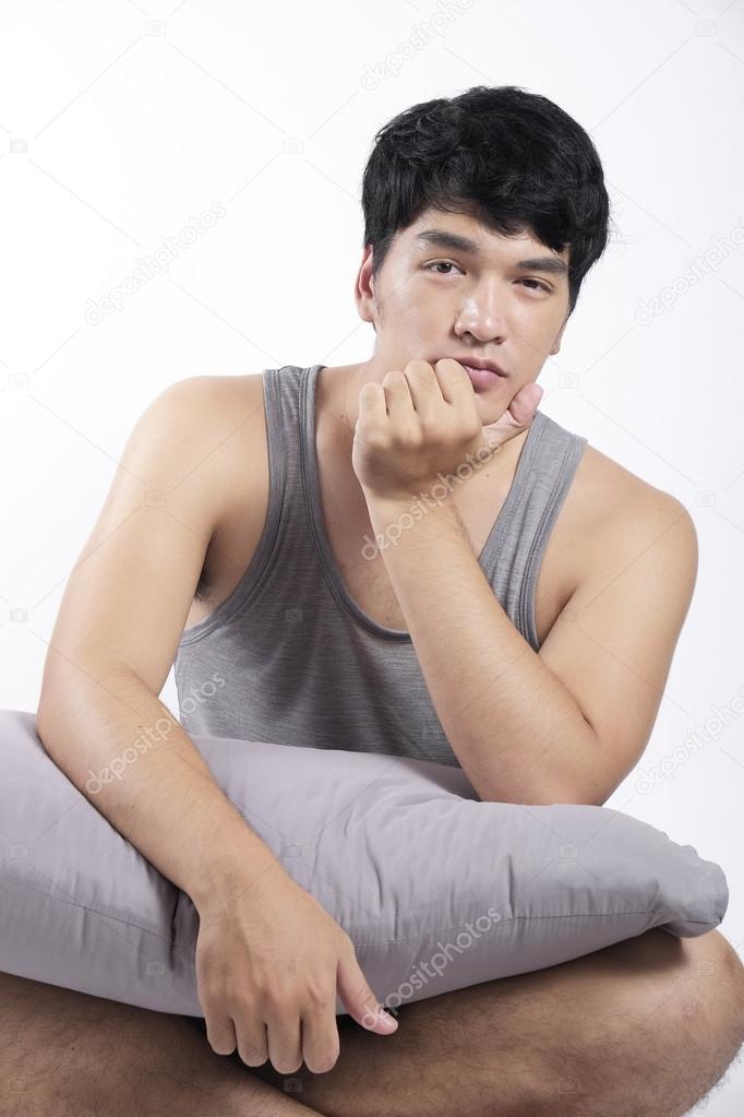 Asian man in grey pajamas sitting and holding the pillow