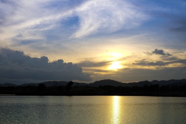 Gün batımında göl ve tepenin arkasında akşam vakti