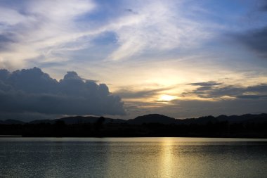 Gün batımında göl ve tepenin arkasında akşam vakti