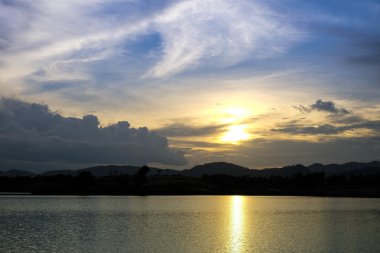 Gün batımında göl ve tepenin arkasında akşam vakti