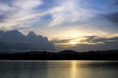 Gün batımında göl ve tepenin arkasında akşam vakti