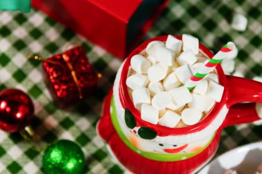 Sıcak çikolata ve marşmelovla dolu seramik kardan adam bardağı, çizgili kamış, süsler, ahşap yüzeyde kardan yapılmış kumaş, şenlikli kış kutlaması için konforu.