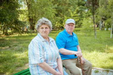 Üst düzey çift baston ile bir parkta bankta oturuyor. Yaşlı çift açık havada rahatlatıcı bir yaz gününde.