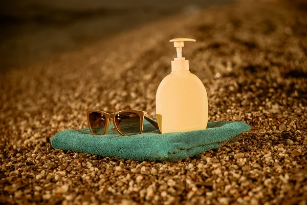 Towel, sunglasses and cream on the beach — Stok fotoğraf