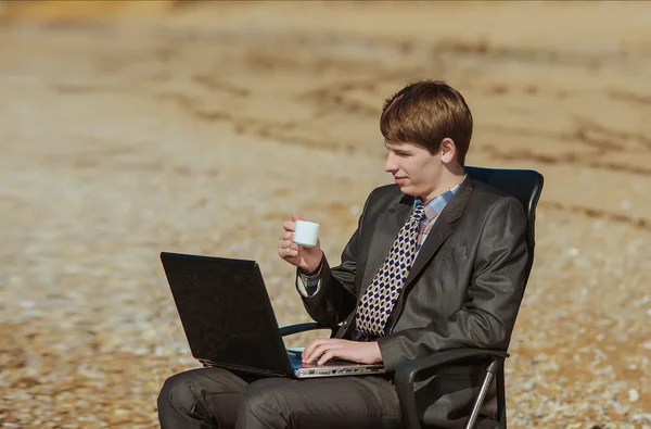 Jovem empresário com uma xícara de café em uma cadeira de escritório no — Fotografia de Stock