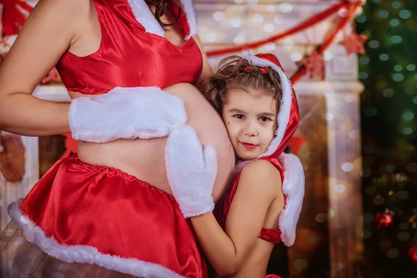 O femeie însărcinată şi o fetiţă cu pălărie de Moş Crăciun. Anul Nou — Fotografie, imagine de stoc