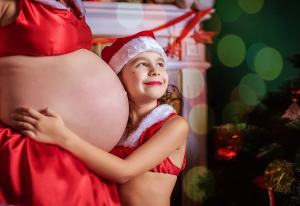 Zwangere vrouw en een klein meisje in een hoed van de Kerstman. Nieuwjaar — Stockfoto