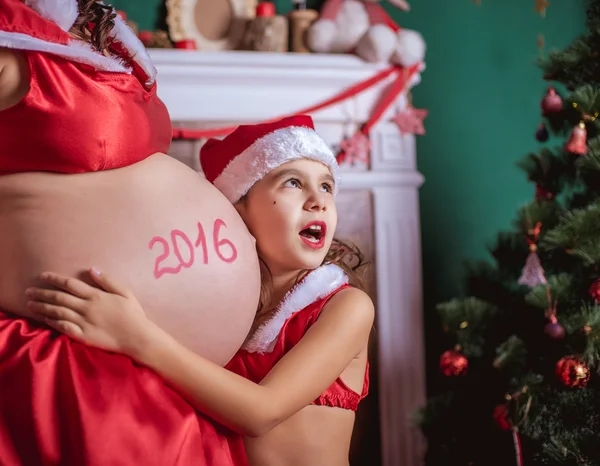 O femeie însărcinată şi o fetiţă cu pălărie de Moş Crăciun. Anul Nou — Fotografie, imagine de stoc